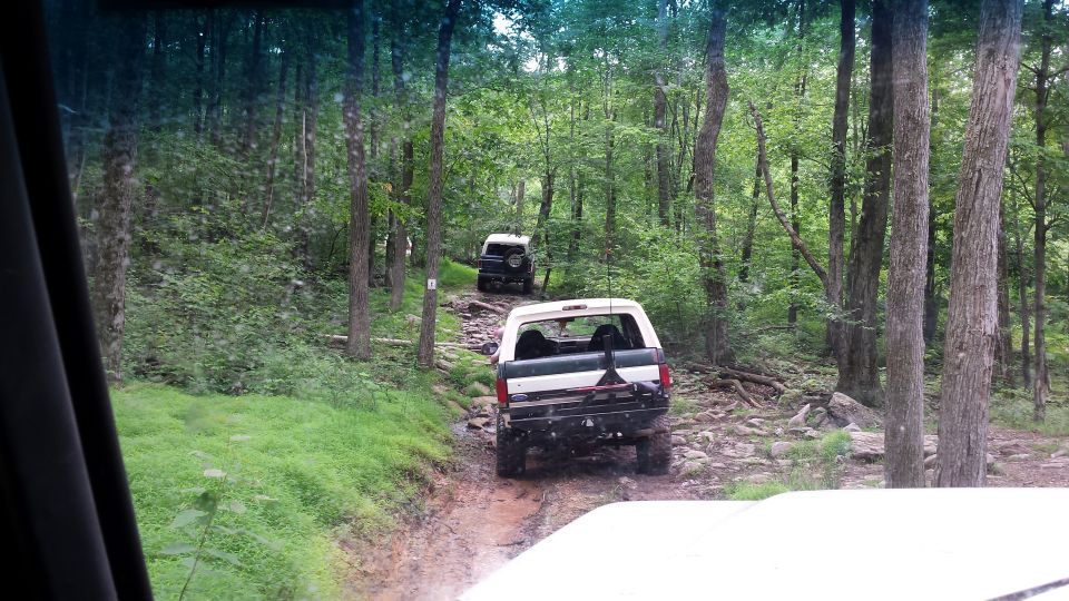 White Ford Bronco driving on a rocky, wooded trail with another Bronco behind it
