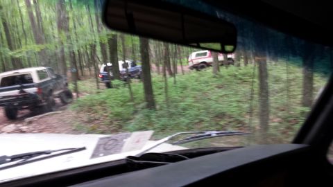 1979 Ford Bronco - Multiple SUVs navigate a wooded trail, with one vehicle in the foreground and others further up the incline.