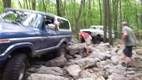 1979 Ford Bronco - A blue SUV navigates a challenging rocky trail with another vehicle visible in the background.