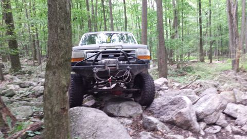 1979 Ford Bronco - A heavily modified truck navigates a rocky trail through a dense forest.