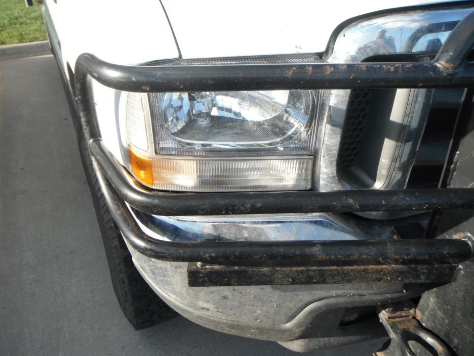 Front of a white Ford truck, showing the headlight, grille, and a black bull bar