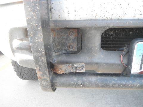 2000 Ford F-250 - The front bumper and brush guard of a truck show signs of wear and tear, with visible rust on the attachment points.