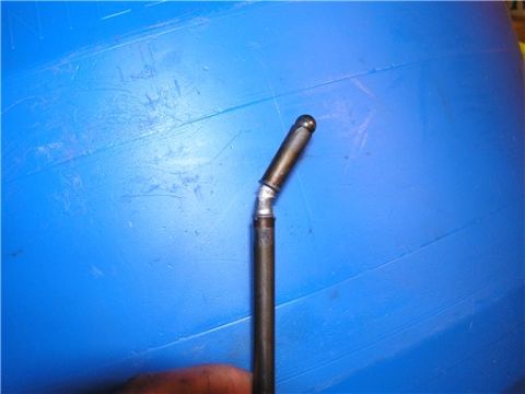 1993 Ford Bronco - A close-up view of a bent metal rod with a rounded tip, set against a textured blue background.