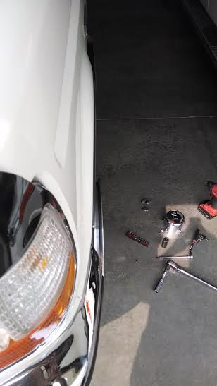 1994 Ford Bronco - Close-up of a white SUV's front fender and headlight assembly, with tools scattered on the floor nearby.