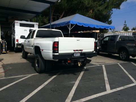 1997 Dodge 3500 - A white dually pickup truck is parked next to a gray pickup truck under a blue awning.