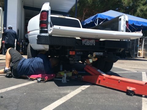 1997 Dodge 3500 - A mechanic works on the underside of a white Dodge Ram pickup truck, with another truck in the background.