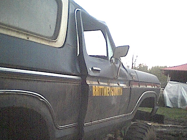 Dark blue 1978 Ford Bronco side view with 'BRITTNEYSMITH' painted in yellow on the door, parked outdoors