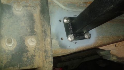 1996 Ford Bronco - A close-up view of a custom black metal bracket welded and bolted to the underside of a vehicle frame. The bracket is attached with four he…