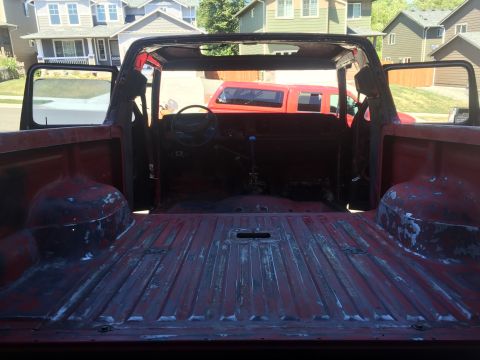 1978 Ford Bronco - The interior and bed of a red pickup truck are shown from a rear-facing perspective. The truck bed is empty and shows signs of wear, while…
