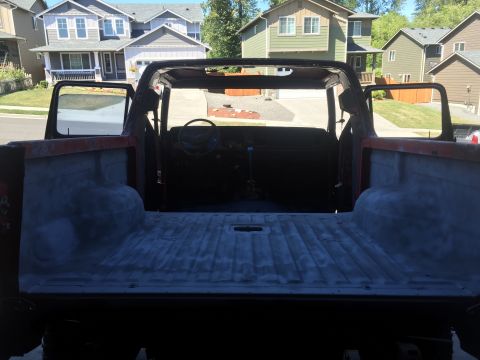 1978 Ford Bronco - The interior and bed of a vintage pickup truck are shown from a rear-facing perspective. The truck bed appears to be prepped for paint, and…