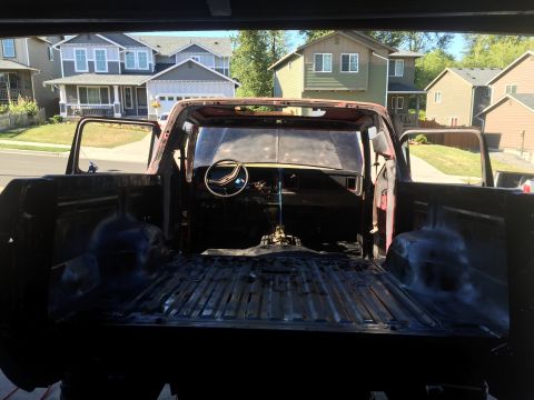 1978 Ford Bronco - View from the rear of a disassembled red pickup truck with doors open, showing the interior and the truck bed. The truck is parked in a dri…