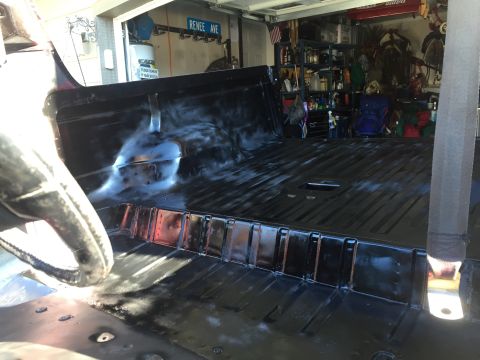 1978 Ford Bronco - The interior of a black vehicle bed is shown with a person's gloved hand in the foreground. The vehicle appears to be in a garage with shel…