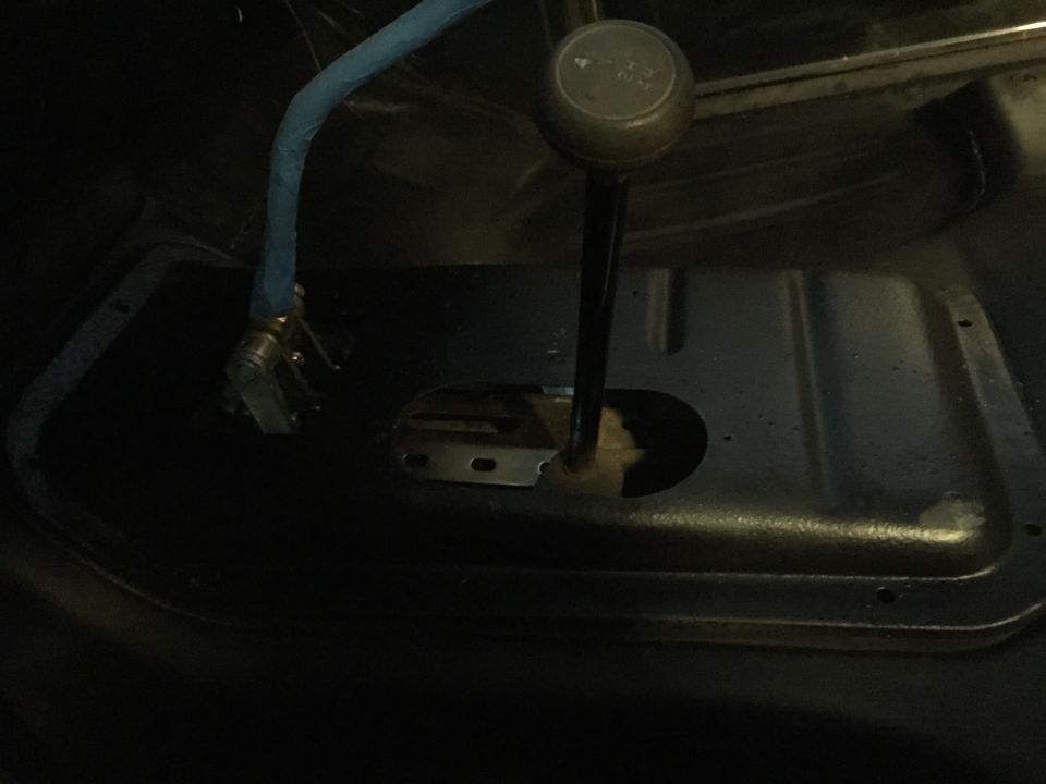 Vintage vehicle interior, manual gear shifter and blue hose on floor console.