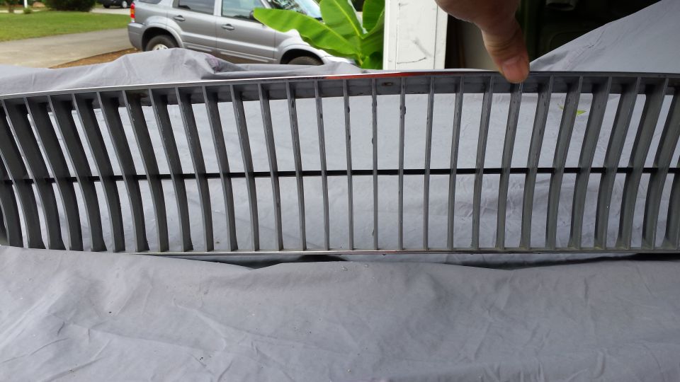 Chrome and black vertical slat grille on a grey tarp, silver SUV in background