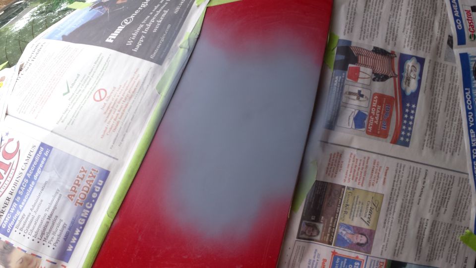 Sanded and primed red car panel with newspapers as masking.