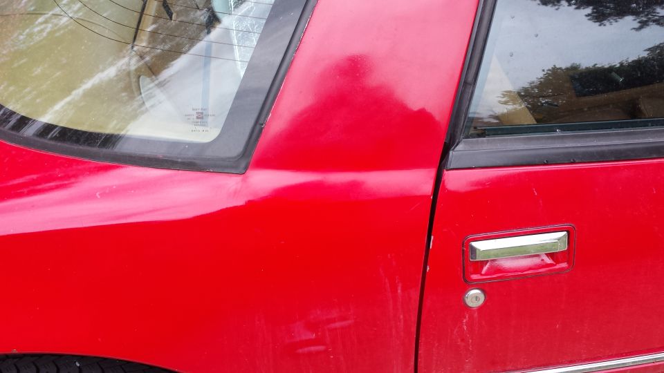 Red car door and rear quarter panel with chrome handle and rear window detail.