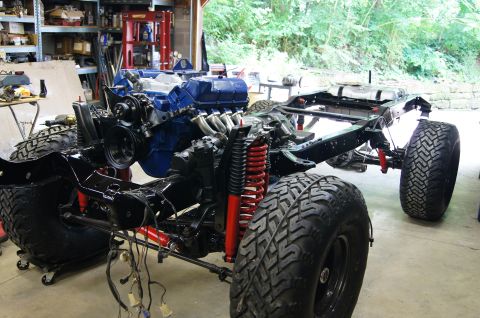 1979 Ford Bronco - The chassis and engine of a vehicle undergoing restoration or modification are shown in a garage setting. The blue engine is prominently di…