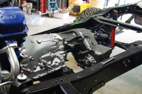 1979 Ford Bronco - A close-up view of a Ford Bronco's transmission and chassis components, painted in gray and black. The blue Ford-branded valve cover is vis…