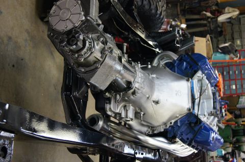 1979 Ford Bronco - A close-up, angled view of a vehicle's powertrain assembly, featuring a transmission, transfer case, and exhaust headers, mounted on a blac…