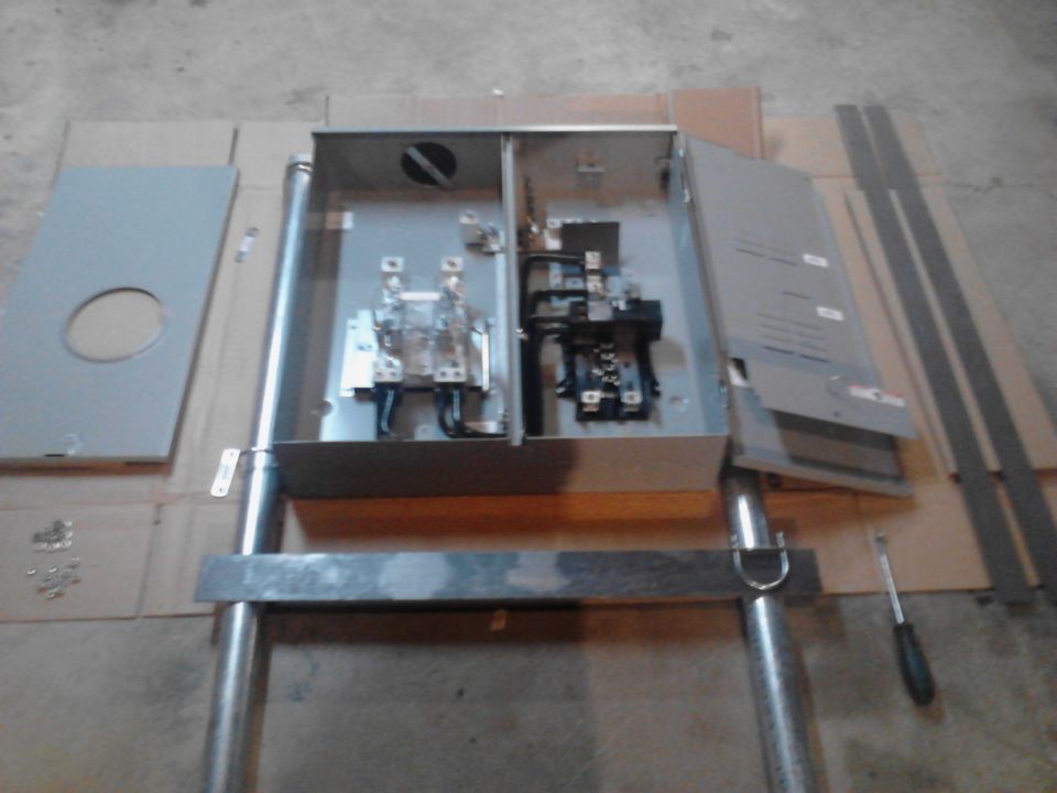 Electrical panel box with breakers and wiring, panel cover, and screwdriver on cardboard.