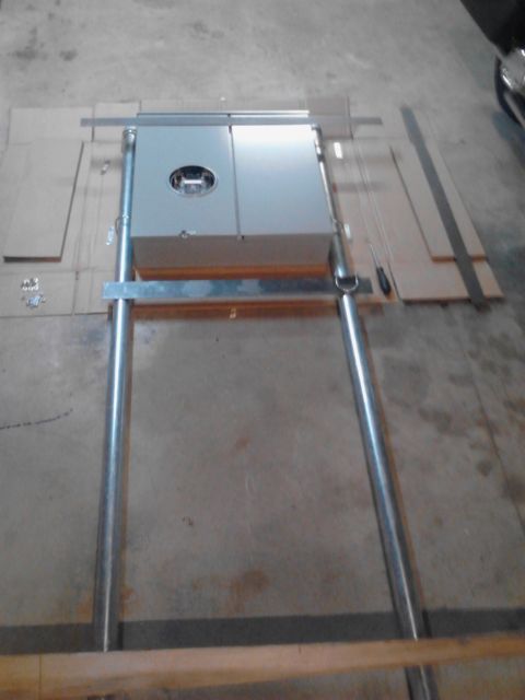 1989 Ford Bronco - A close-up, overhead view of a gray electrical box mounted on a metal frame, resting on a concrete floor. The box has a circular emblem and…