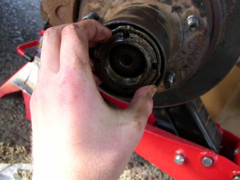 1989 Ford Bronco - A hand is shown removing the hub assembly nut from a vehicle's wheel hub, likely during maintenance or repair.