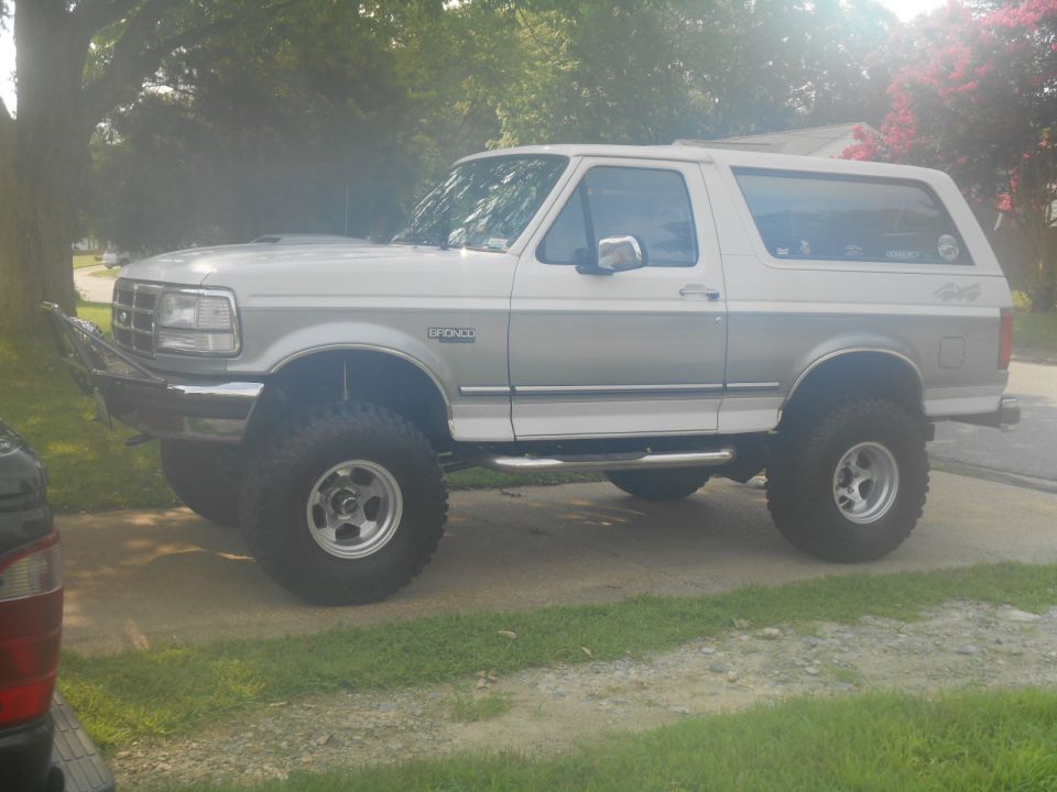 Lifted 1994 Ford Bronco, two-tone silver and white, with custom bumper and large tires.