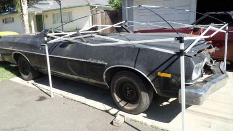 1972 Ford Ranchero - A damaged black 1972 Ford Ranchero sits in a driveway under a canopy, with another vehicle visible behind it.