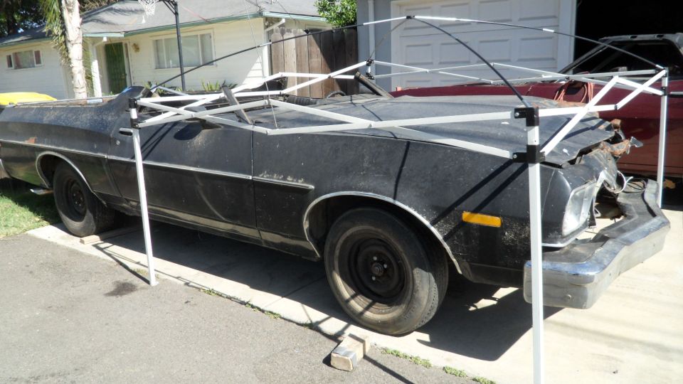 Black 1972 Ford Ranchero with front-end damage, covered by a canopy