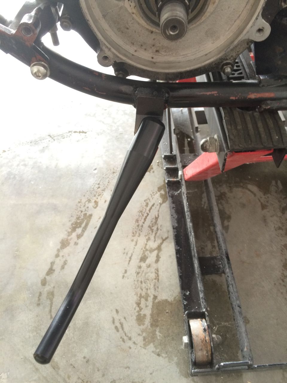 Motorcycle kickstand extended, attached to frame near engine