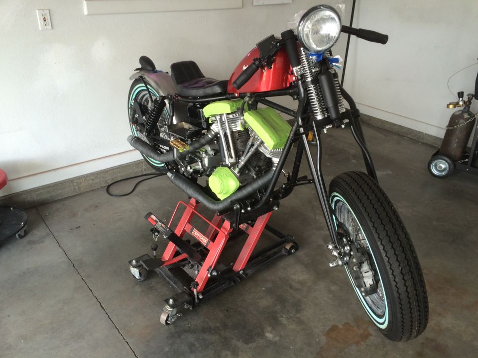 Motorcycle on a red lift with green padding on the engine. Red gas tank, black seat, and black exhaust pipes
