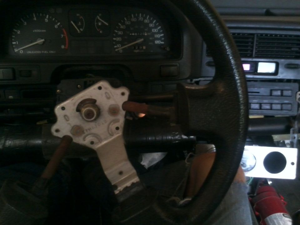 Car interior showing dashboard gauges and a disassembled steering column