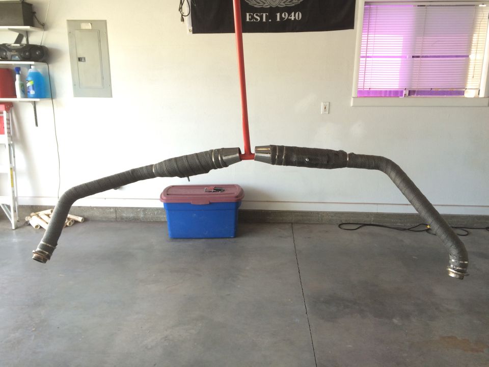 Two black motorcycle exhaust pipes with heat wrap, suspended by a red pole