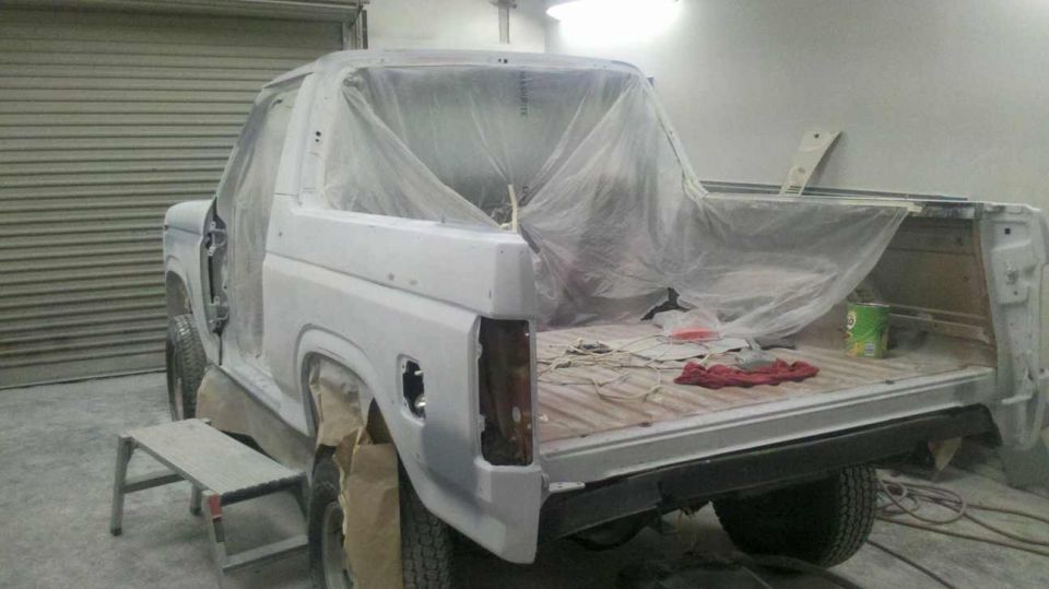 Ford Bronco with doors removed, covered in primer and plastic sheeting, in a workshop