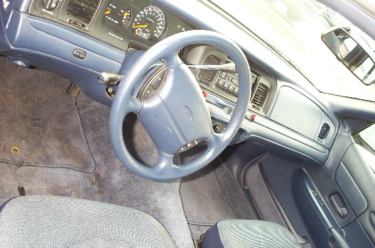 Blue-gray interior of a Ford Crown Victoria showing steering wheel, dash, and center console from driver's side