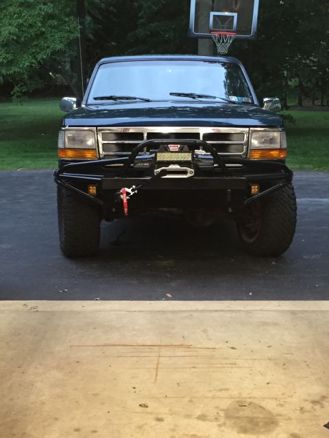1994 Ford Bronco - A dark blue Ford Bronco is parked in a driveway, facing the camera, with a basketball hoop in the background.
