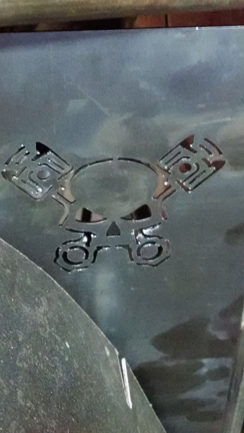 1985 Jeep CJ7 - A custom skull and piston emblem is cut into a dark metal panel, suggesting a personalized automotive part.