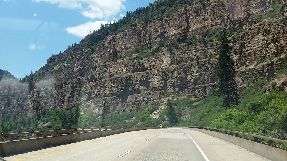 Roadway alongside a steep, layered cliff face with trees
