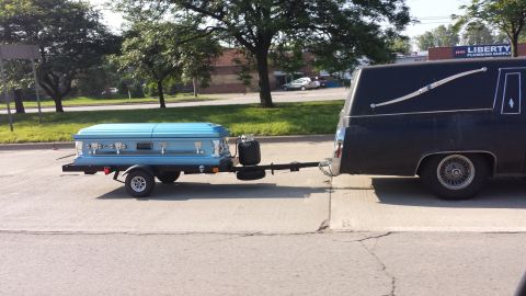 1995 Ford Bronco - A hearse is seen towing a blue coffin on a small trailer.