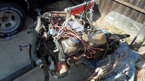 1972 Ford Ranchero - Engine assembly suspended by chains, with a tire and windshield in the background.