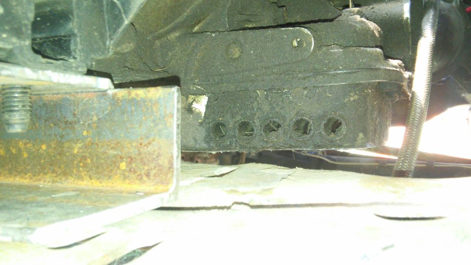 Close-up of rusty metal bracket and dark mechanical component with circular openings