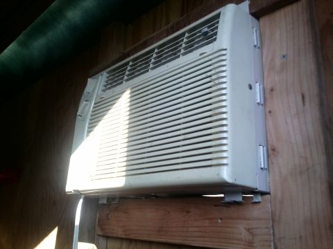 1991 Honda CRX - A window air conditioning unit is mounted on a wooden wall, with sunlight casting shadows.
