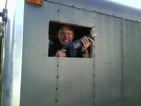 1991 Honda CRX - A man with a menacing grin holds a reciprocating saw while looking out of a small window in a metal structure.