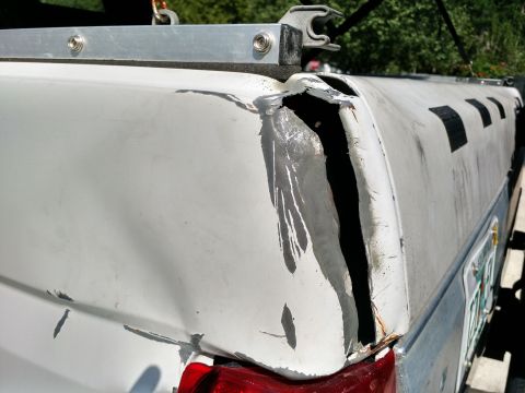 1992 Ford Bronco - The rear section of a truck bed cap has sustained significant damage, with a large opening exposing the interior structure.