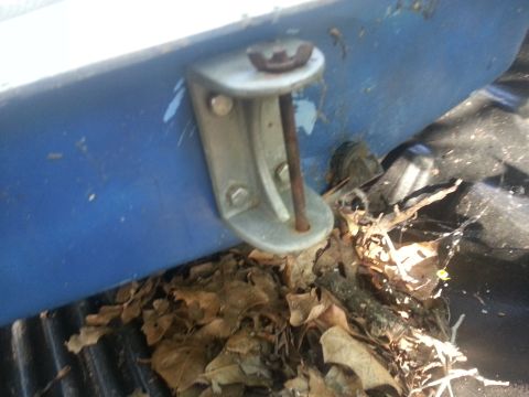 1973 Ford F-100 - A close-up view of a blue surface with a metal bracket and bolt, surrounded by debris.