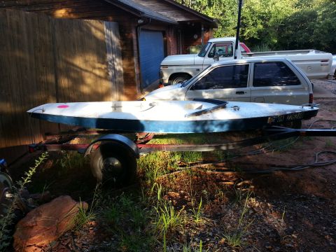 1973 Ford F-100 - A white 1973 Ford F-100 pickup truck is visible behind a boat on a trailer, parked in front of a wooden garage.