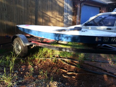 1973 Ford F-100 - A boat is loaded onto a trailer, with a car partially visible behind it.