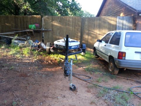 1973 Ford F-100 - A white hatchback is parked next to a boat on a trailer in a yard with a wooden fence.