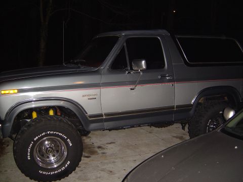 1986 Ford Bronco - This lifted 1986 Ford Bronco is parked outdoors at night, showing its two-tone paint and prominent mud-terrain tires.