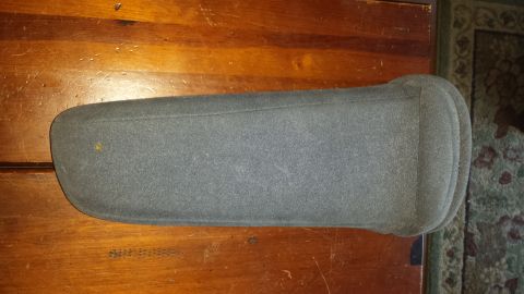 1995 Ford Bronco - This is a gray fabric armrest, likely from a vehicle's center console, placed on a wooden table.